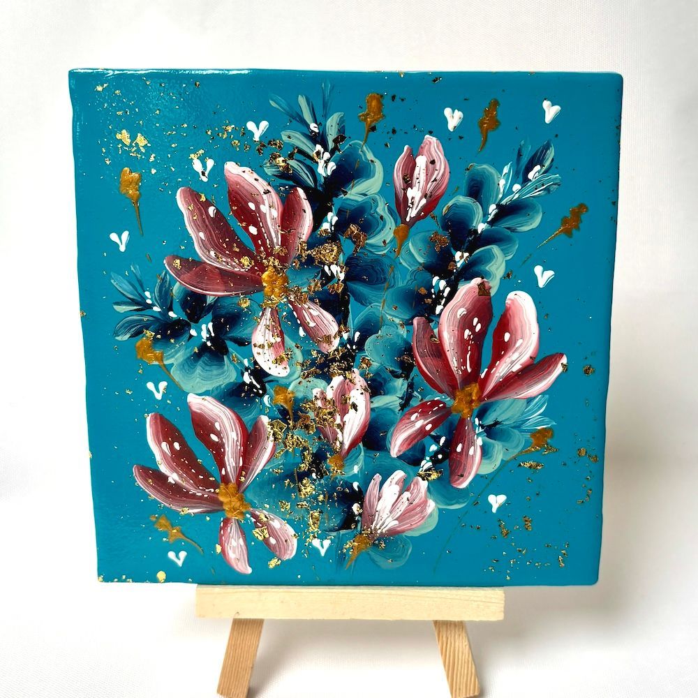 Bloemenschilderij op een turquoise canvas, tentoongesteld op een kleine houten schildersezel.