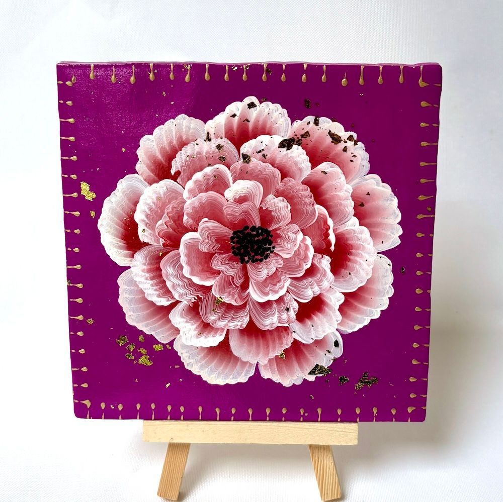 Een roze-witte bloem op een paarse vierkante achtergrond met bladgoudaccenten, rustend op een kleine houten schildersezel.