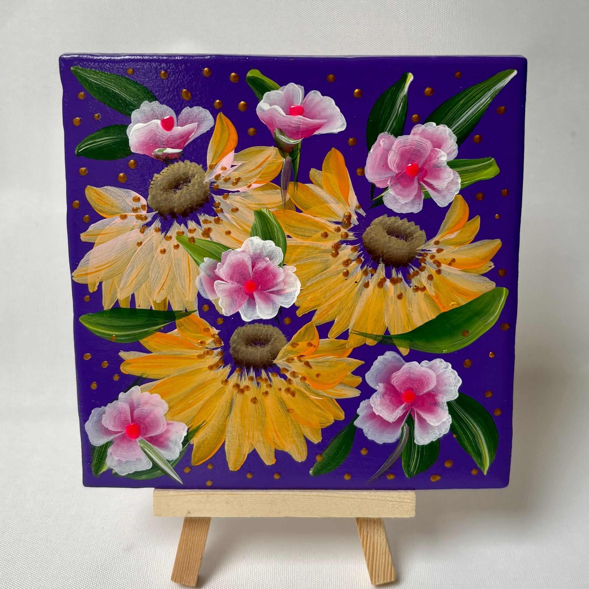 Een klein, vierkant schilderij van gele zonnehoedjes en roze bloemen met groene bladeren op een levendige paarse achtergrond.