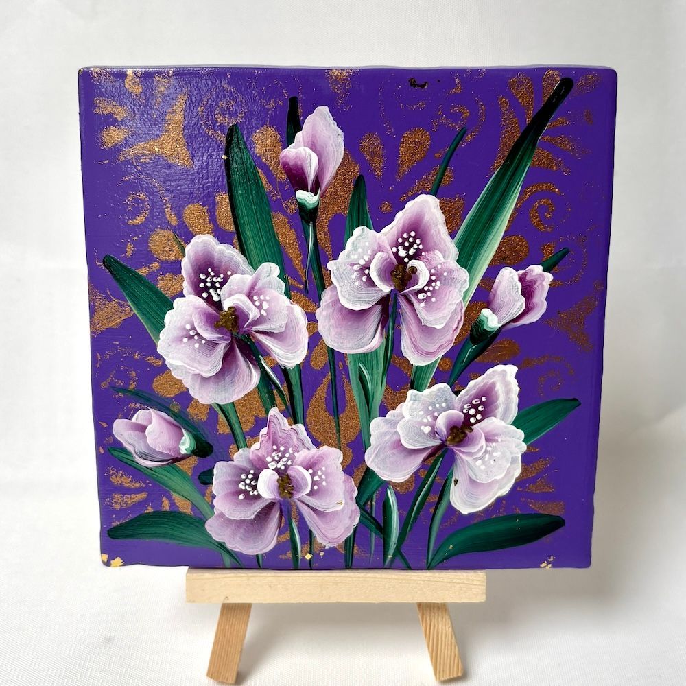 Paars bloemenschilderij op een kleine ezel, met witte en lavendelkleurige bloemen en gouden accenten op een violette achtergrond.
