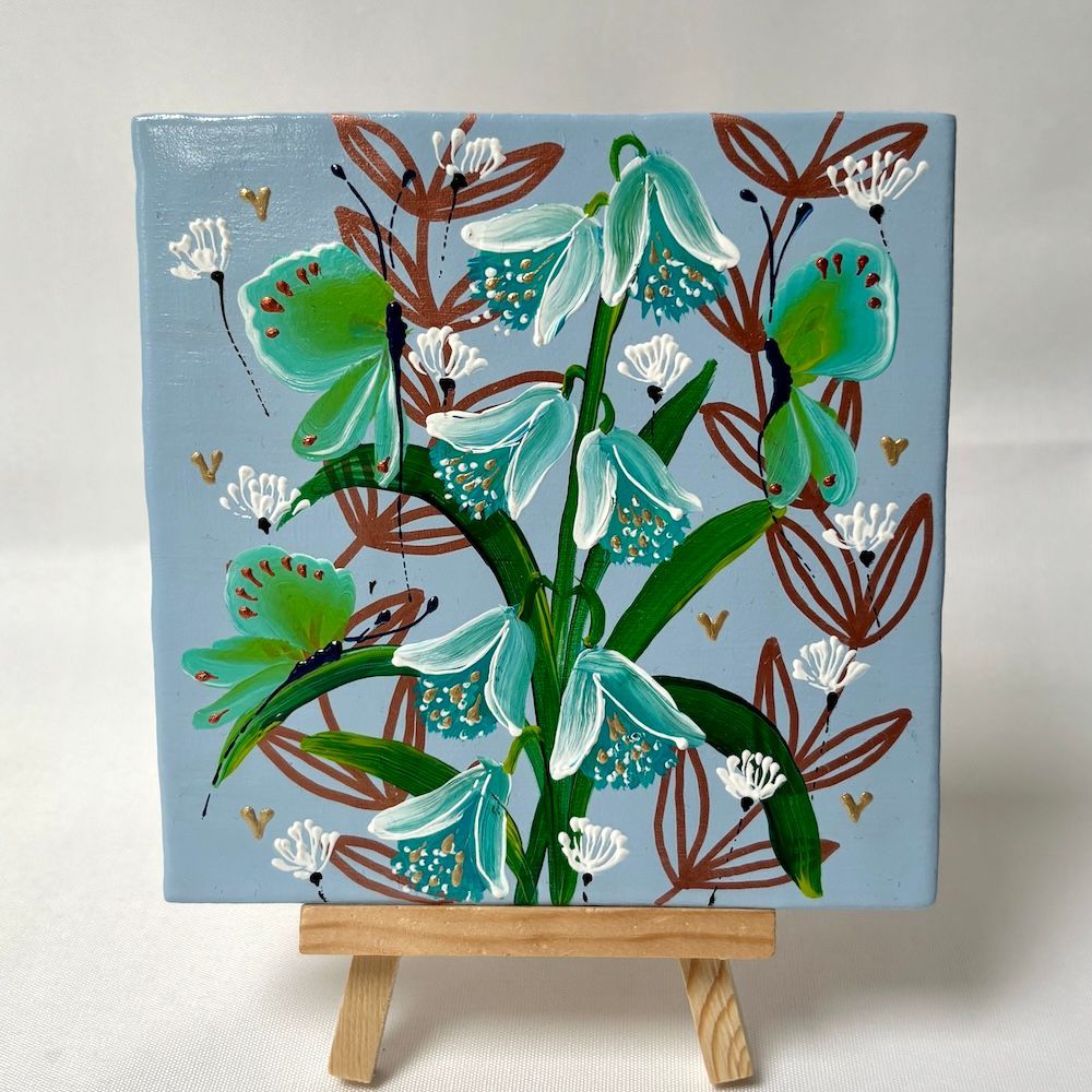 Abstracte bloemenschilderij op een kleine ezel, met turquoise, groene en bruine bloemen op een lichtblauwe achtergrond.