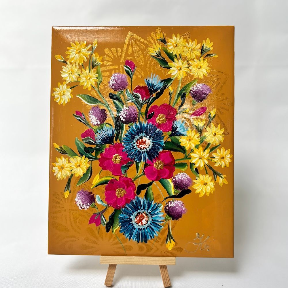 Een tegel van kleurrijke wilde bloemen in tinten geel, blauw en roze op een goudkleurige, gestructureerde achtergrond