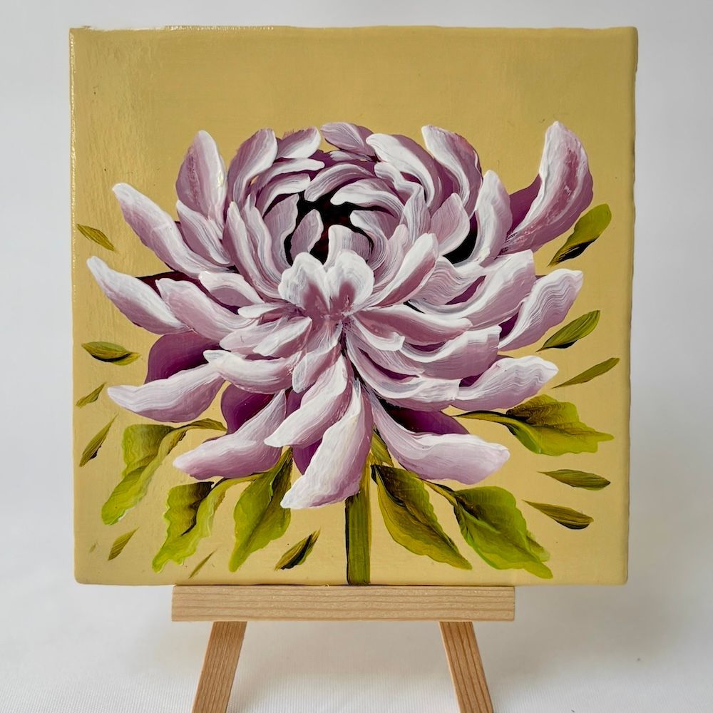 Een schilderij van een lichtpaarse chrysant op een gele achtergrond, rustend op een kleine houten schildersezel.