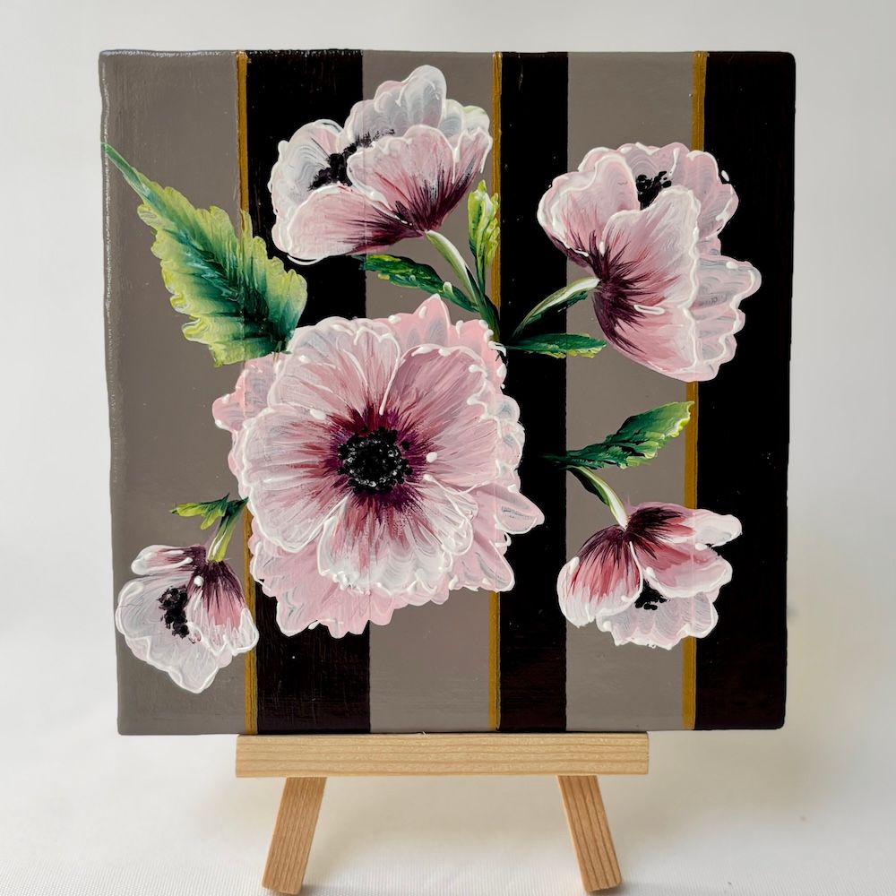 Roze bloemen schilderij op een klein canvas schildersezel met een zwart-goud gestreepte achtergrond.