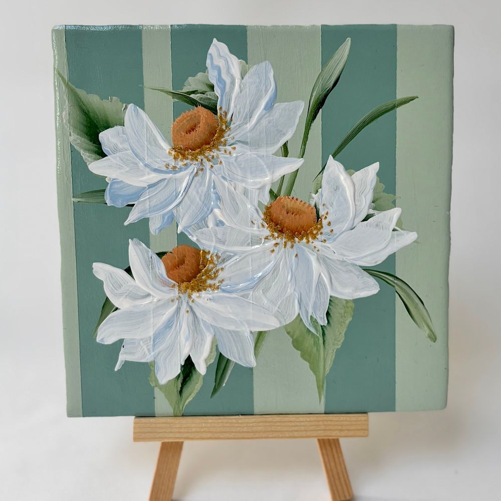 Een vierkant tegeltje van witte madeliefjes met bruine hartjes op een verticaal groen saliegroene gestreepte achtergrond.