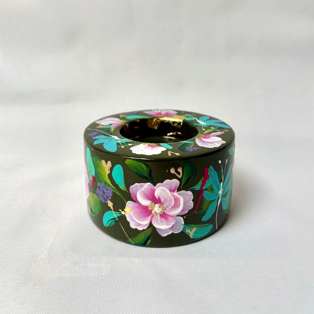 Een cilindrische, donkergroene kaarsenhouder versierd met handgeschilderde roze bloemen, groene bladeren en gouden accenten.