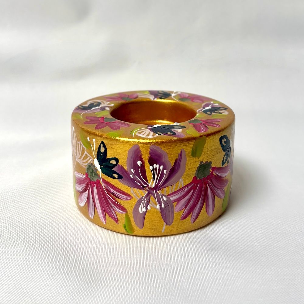 Een goudkleurige kaarsenhouder versierd met handgeschilderde paarse bloemen en zwarte vlinders.