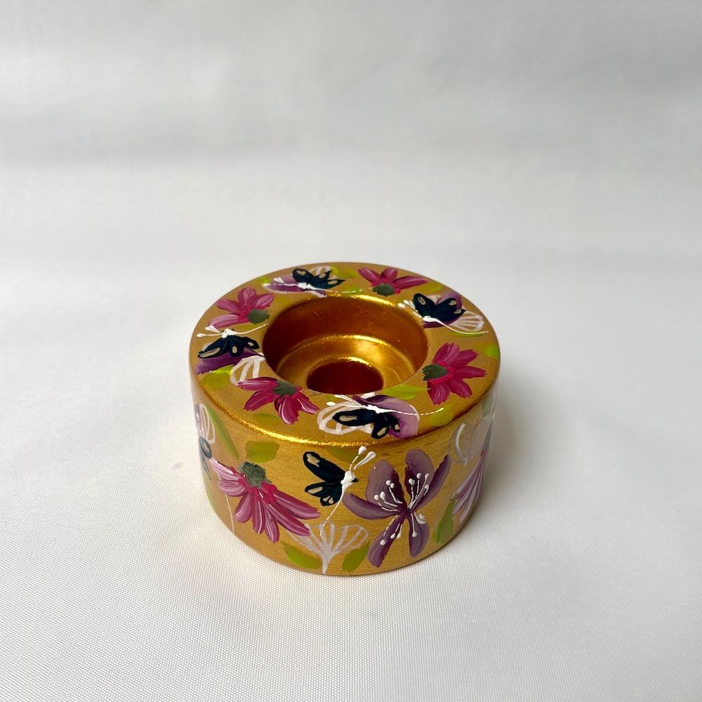 Een goudkleurige kaarsenhouder versierd met handgeschilderde paarse bloemen en zwarte vlinders.