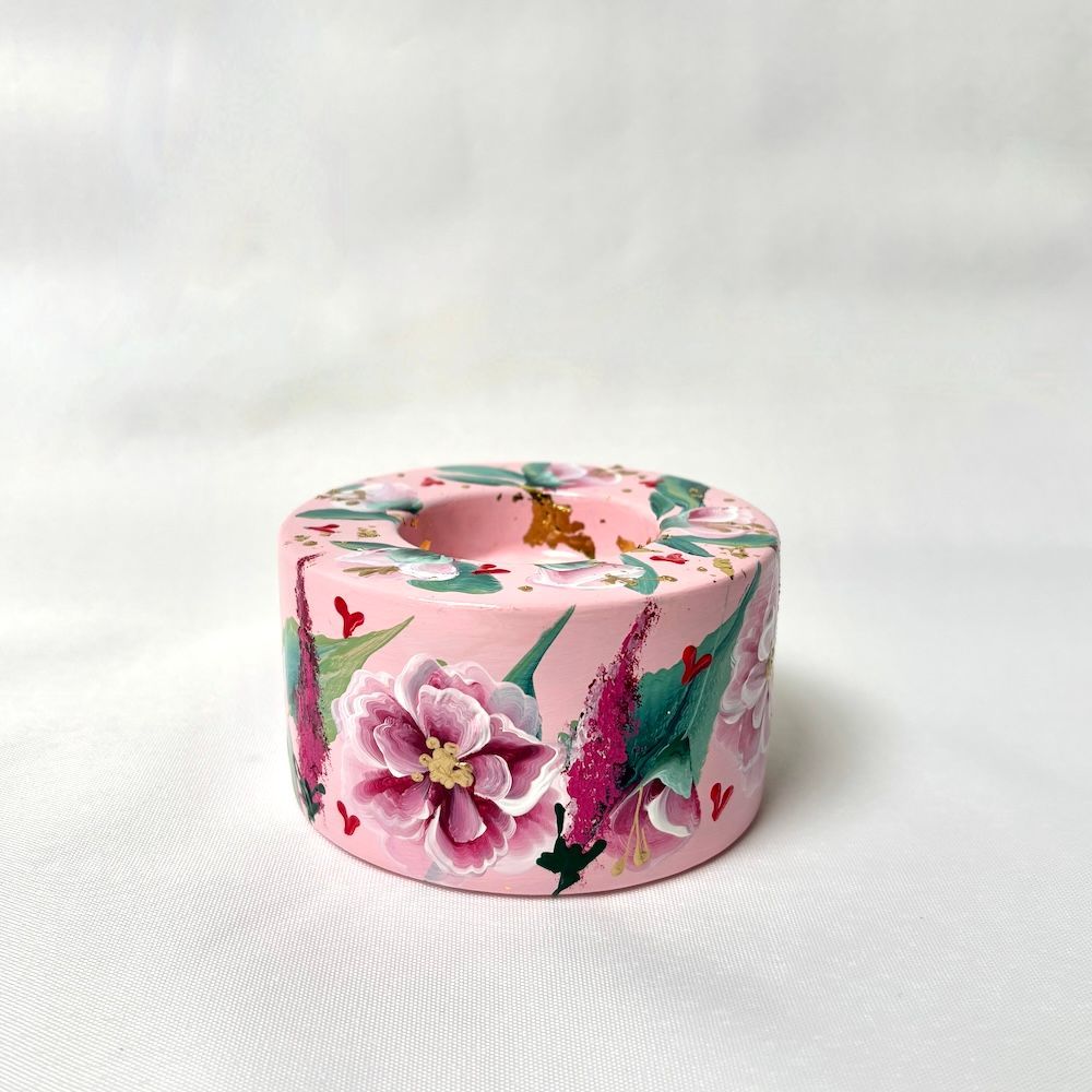 Een lichtroze betonnen kaarsenhouder, handbeschilderd met gedetailleerde roze bloemen, groene bladeren en gouden accenten.