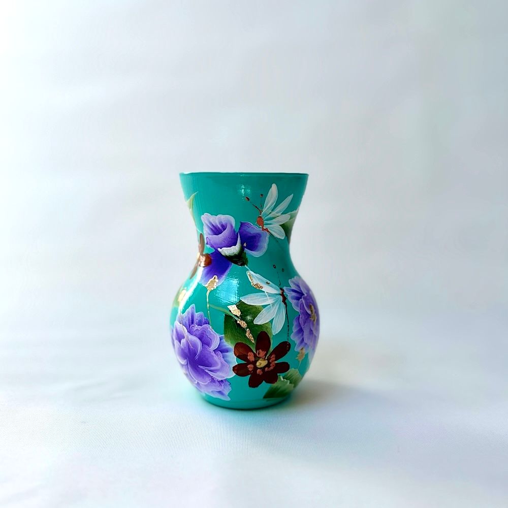 Een klein, turquoise vaasje versierd met handgeschilderde paarse bloemen, witte bloesems en een klein donker bloempje.