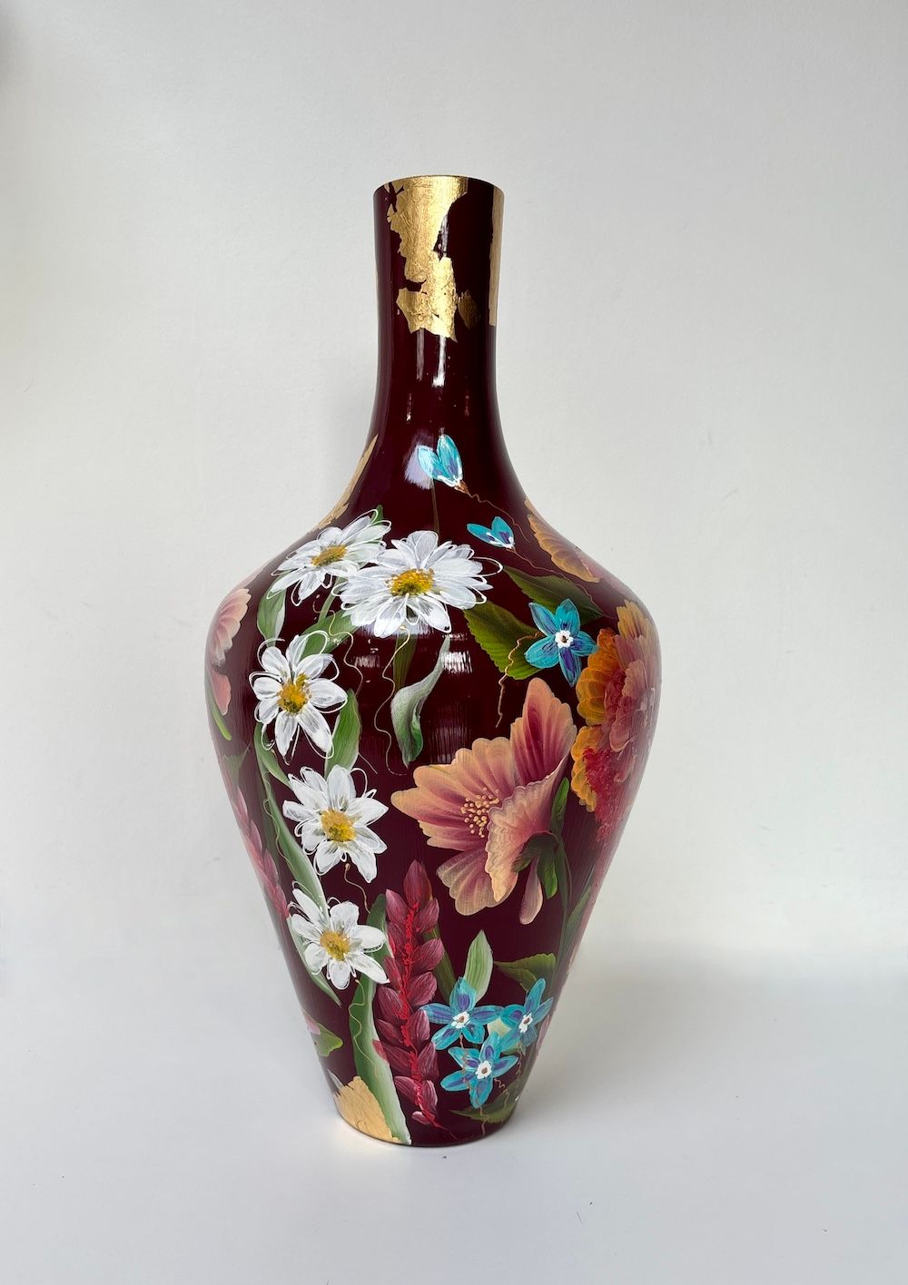 Een dieprode handgeschilderde vaas versierd met kleurrijke, handgeschilderde bloemen, met details van bladgoud aan de rand.