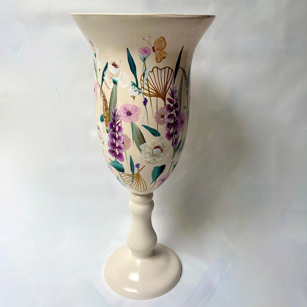 Een crèmekleurige vaas op een voetstuk, beschilderd met paarse bloemen, groene bladeren en gouden vlinder- en bloemaccenten.