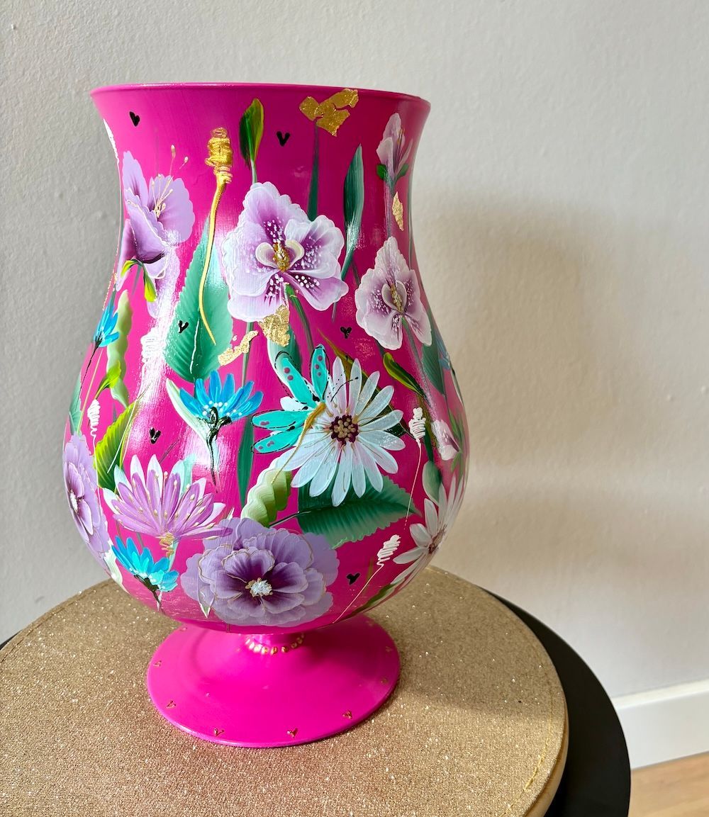 Een levendige, felroze vaas op een voetstuk, versierd met handgeschilderde kleurrijke bloemen in paarse en blauwe tinten.