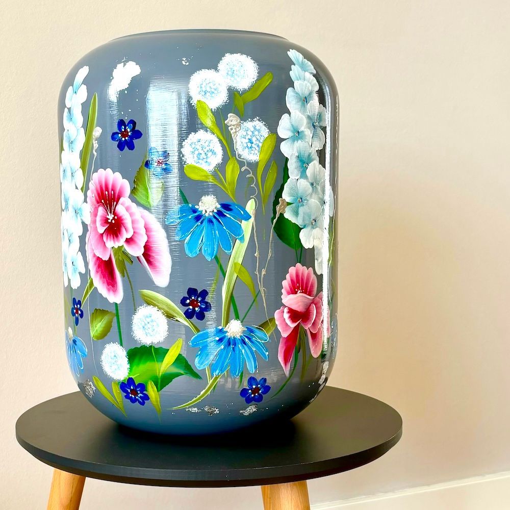 Decoratieve grijze vaas beschilderd met kleurrijke bloemen op een zwarte standaard.