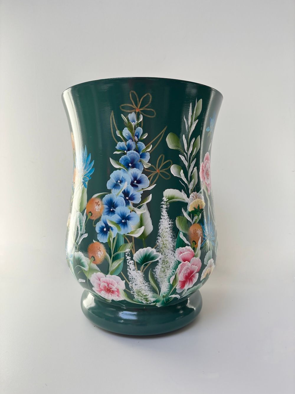 Een donkergroene vaas met een geschilderde grijze kraanvogel met een gele kuif, die naast een blauw bloemstuk staat.