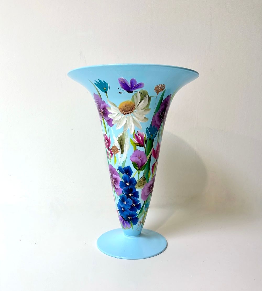 Een lichtblauwe glazen vaas met een uitlopende rand, handbeschilderd met kleurrijke wilde bloemen op een witte achtergrond.