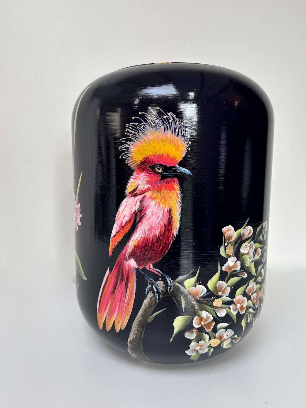 Een glanzende, zwarte, cilindervormige vaas, handbeschilderd met een kuifdragende rode vogel die op een bloeiende tak zit.