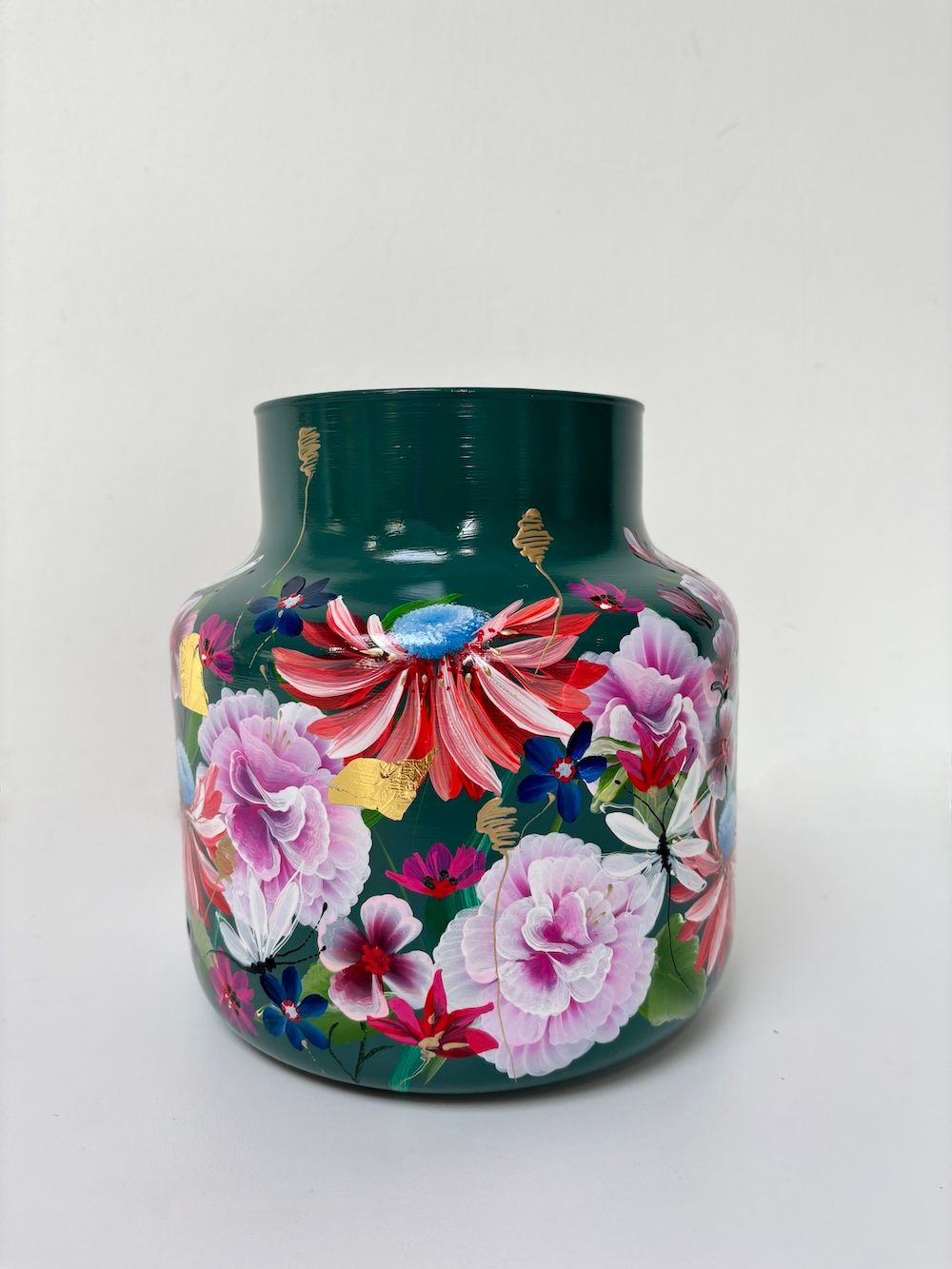 Een donkergroene vaas beschilderd met een levendig, kleurrijk bloemenpatroon van roze, witte en rode bloemen