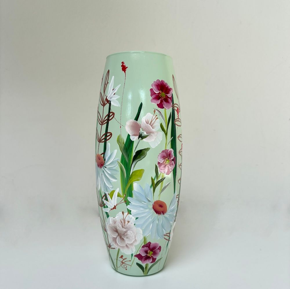Een lichtgroene cilindrische vaas, handbeschilderd met witte madeliefjes, paarse bloemen en delicate groene stengels.