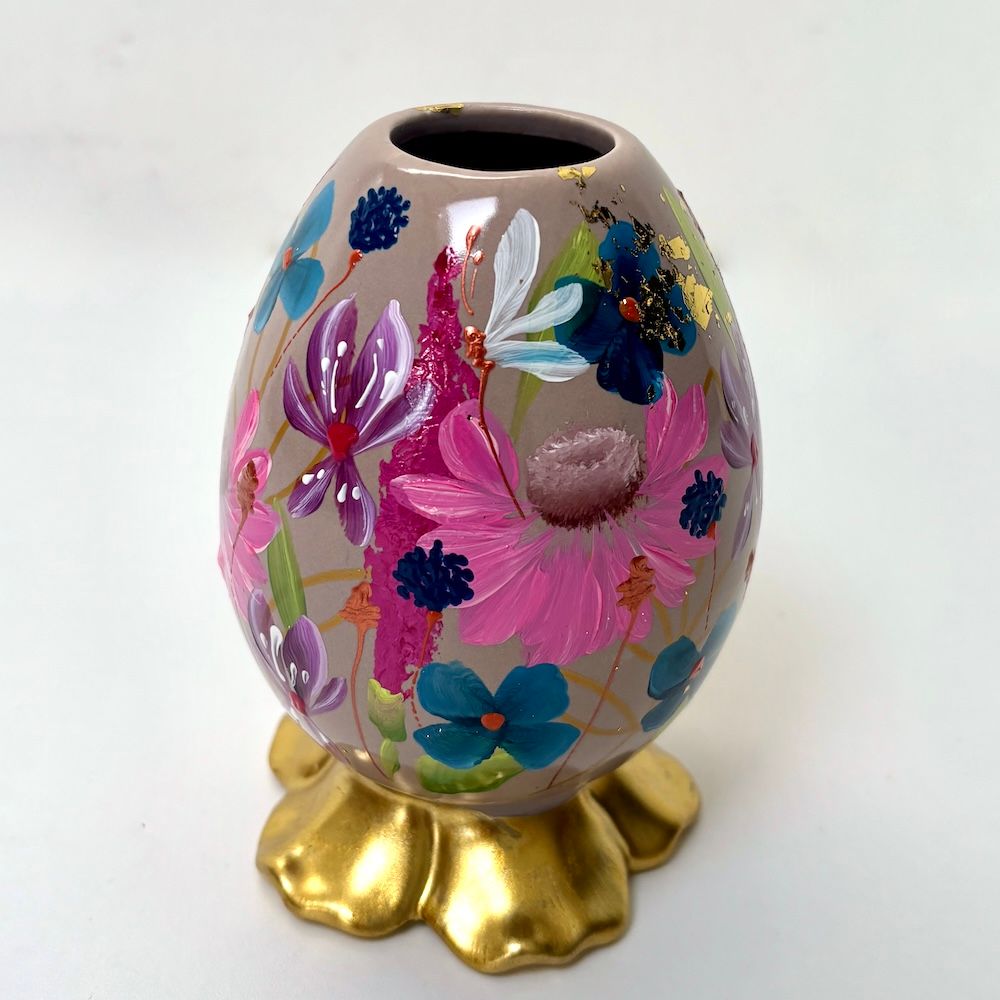 Versierd roze eivormig ornament met kleurrijke bloemmotieven op een gouden standaard
