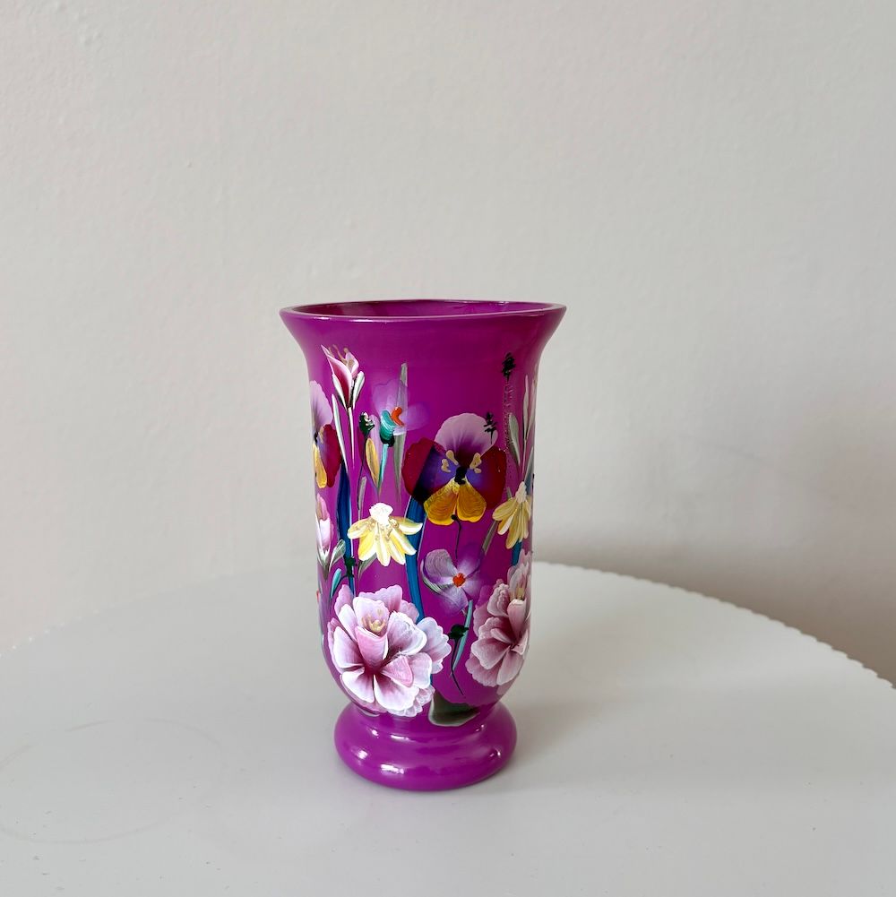 Een felroze vaas, versierd met roze en gele bloemen, staat op een witte ondergrond tegen een effen muur.
