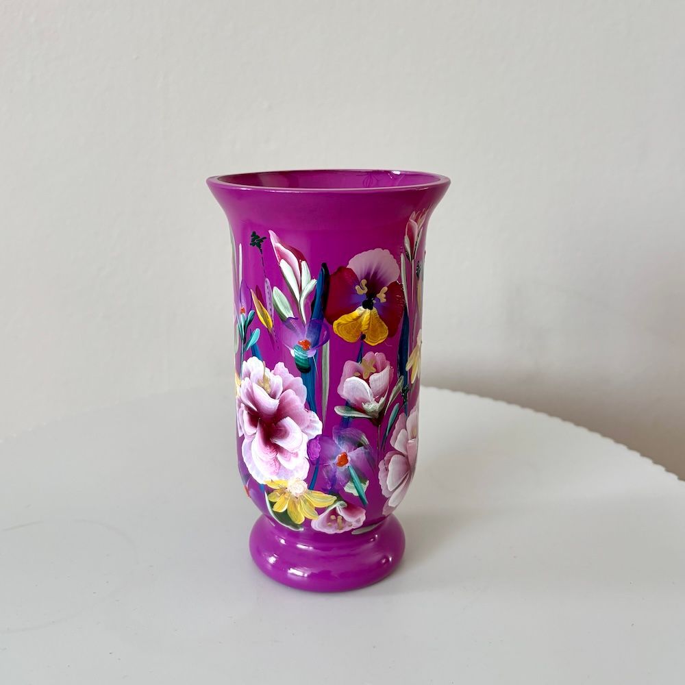 Een felroze vaas, versierd met roze en gele bloemen, staat op een witte ondergrond tegen een effen muur.