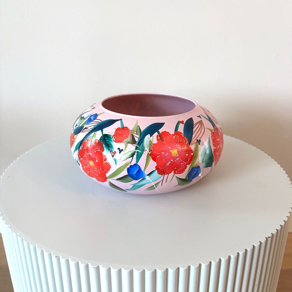 Roze keramische schaal met bloemenmotief op een witte geribbelde voet tegen een effen achtergrond.