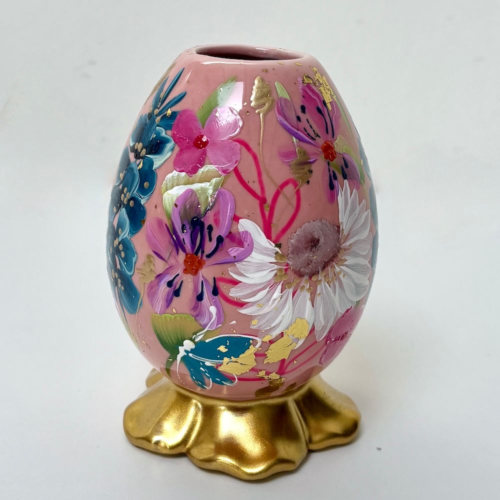 Roze, bloemrijk, eivormig decoratief object op een gouden voetstuk.