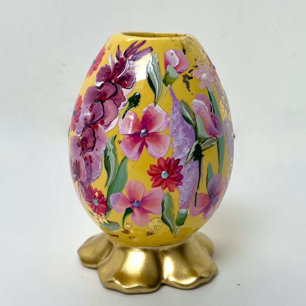 Gele, eivormige vaas met bloemenmotief op een gouden, bloemvormige voet.