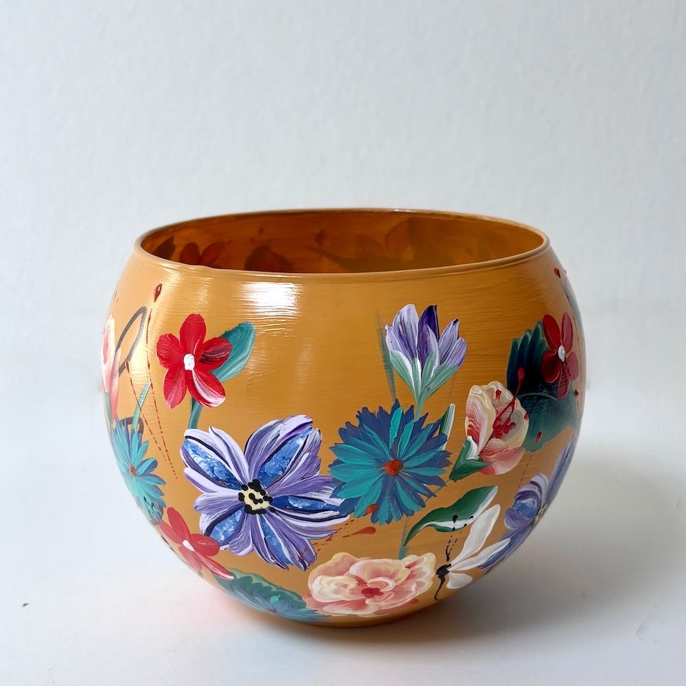 Handbeschilderde oranje kom met kleurrijke bloemmotieven op een witte achtergrond.