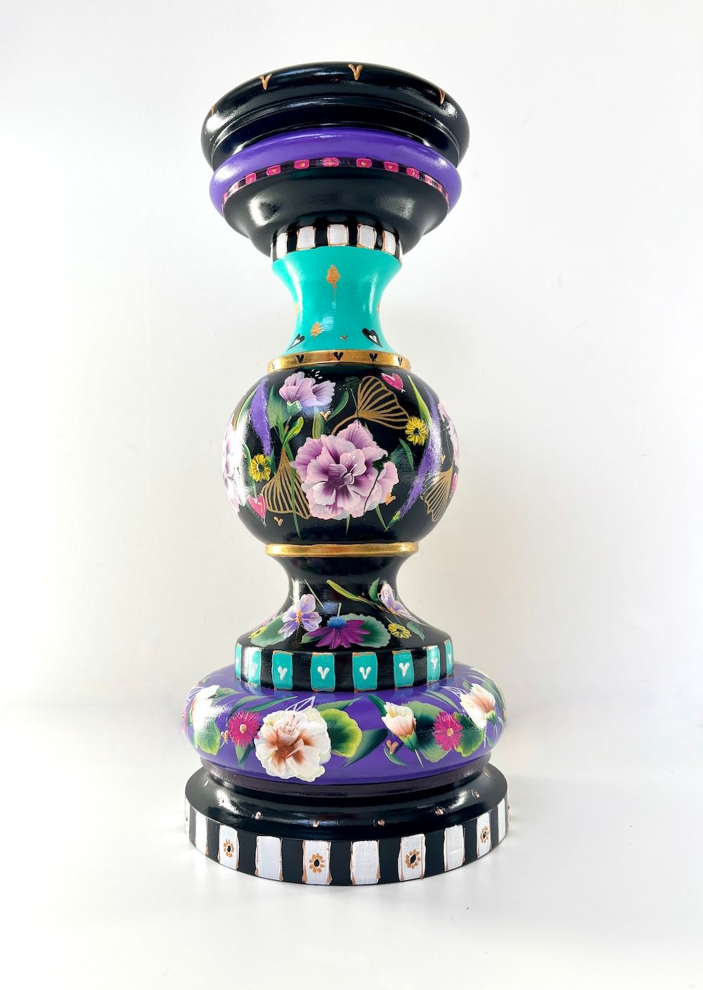 Een decoratieve, handbeschilderde houten kaarsenhouder met bloemen, opvallende strepen en paarse en turquoise tinten.