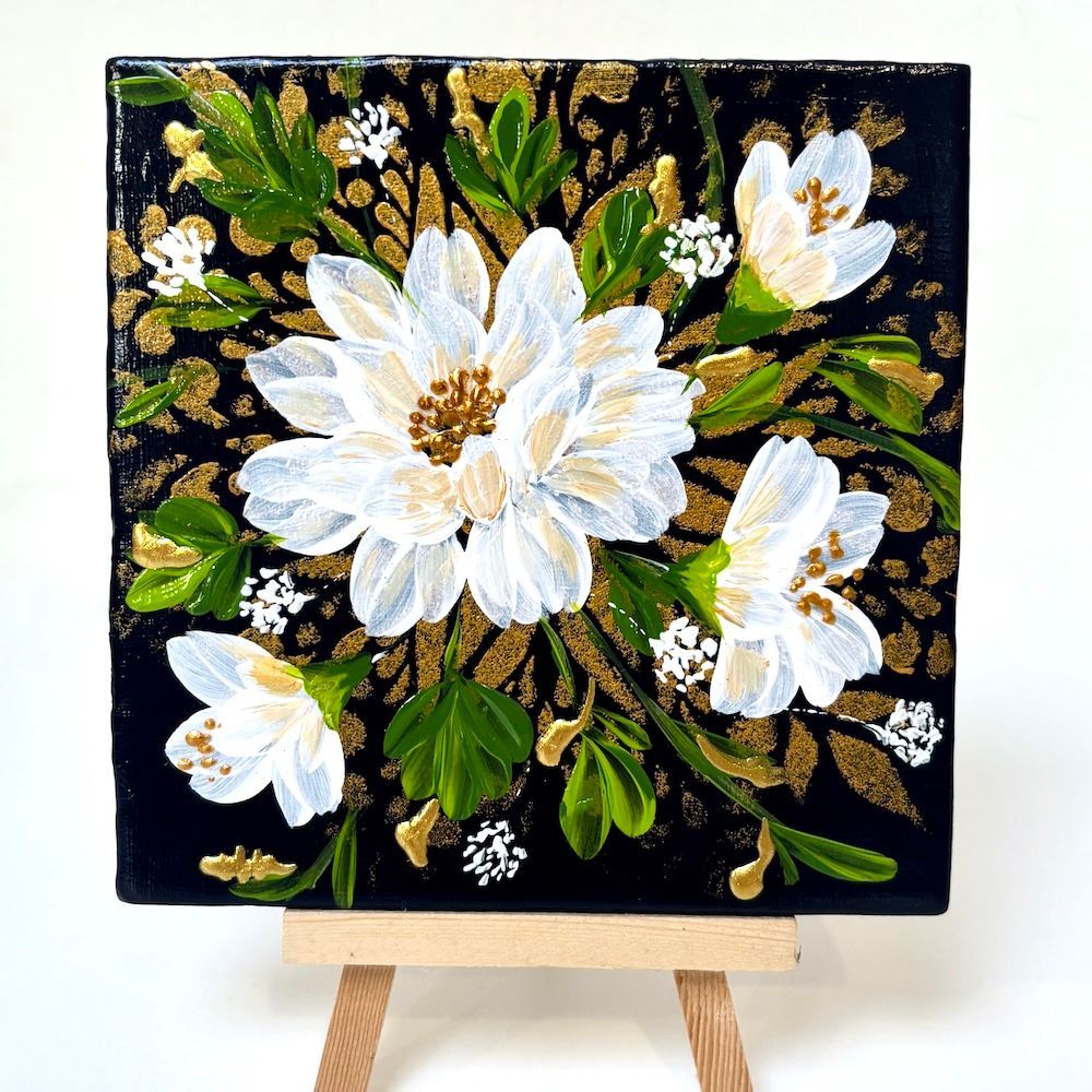 Een schilderij met witte bloemen op een zwarte achtergrond, tentoongesteld op een kleine houten schildersezel.