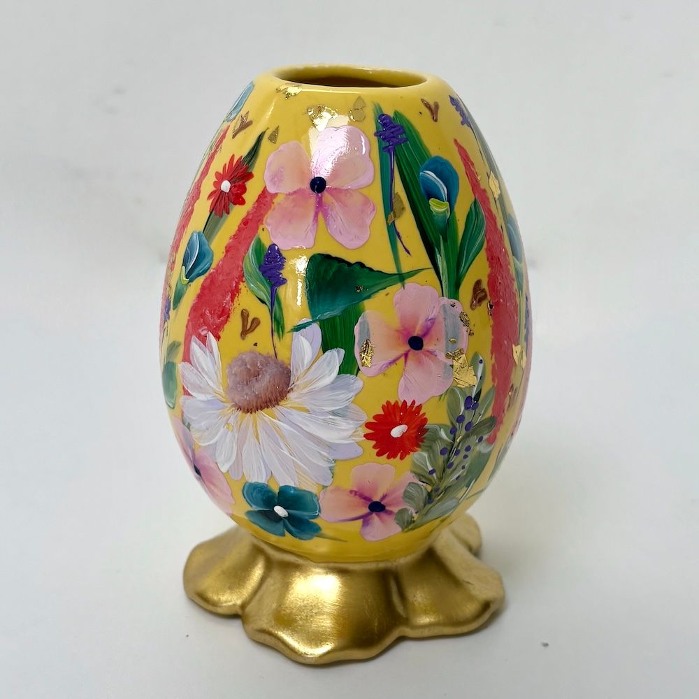 Decoratieve gele eivormige vaas met handgeschilderde roze en witte bloemen op een gouden voet.