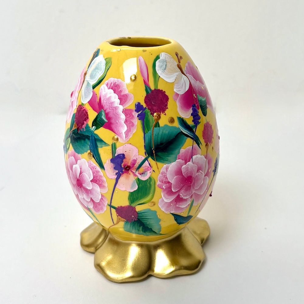 Een gele, eivormige vaas versierd met geschilderde roze en witte bloemen rustend op een gouden, geschulpte voet.