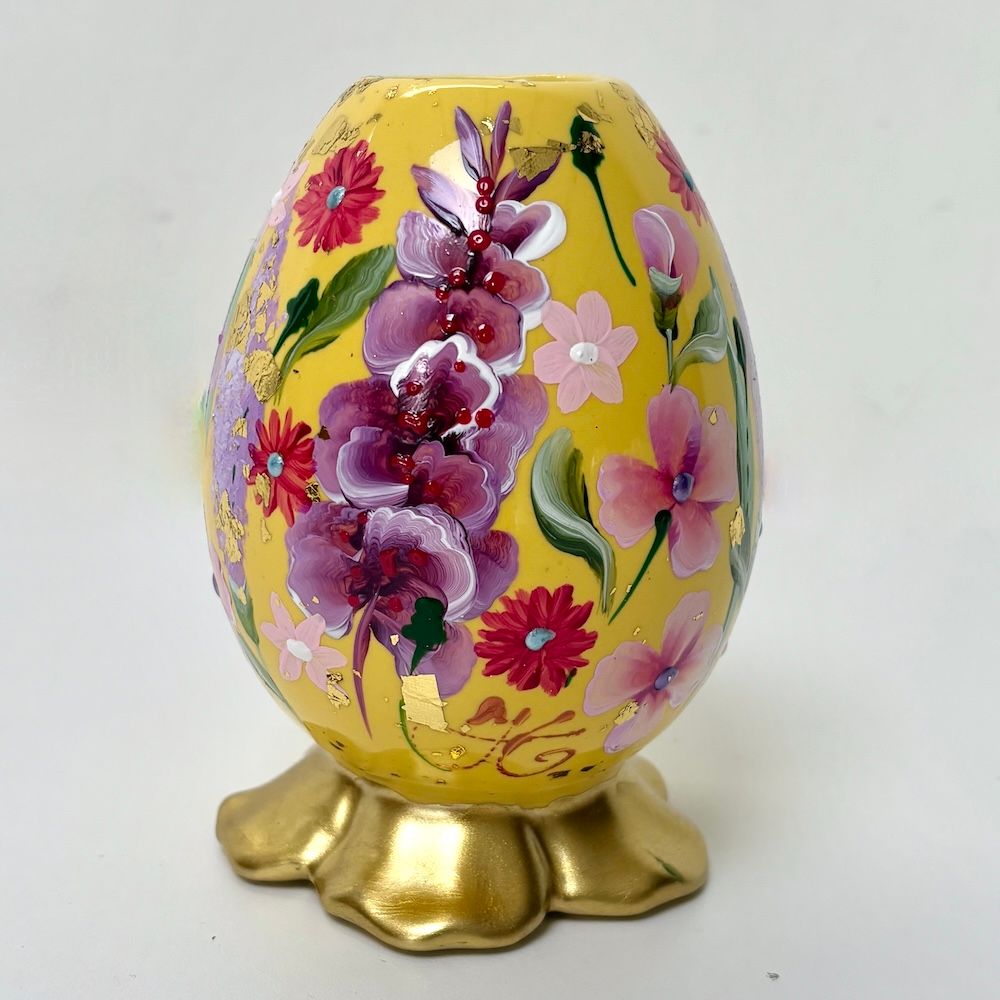Gele, eivormige vaas met bloemenmotief op een gouden, bloemvormige voet.