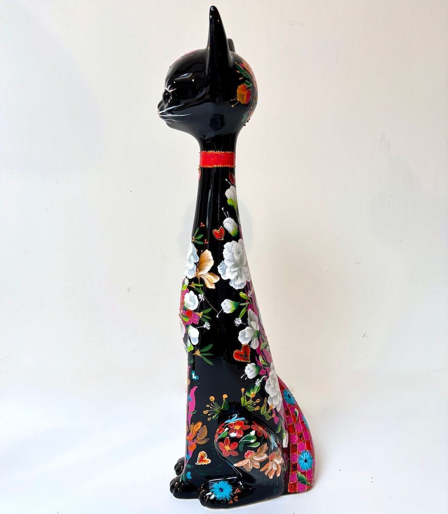 Decoratieve sculptuur van een zwarte kat met kleurrijke bloemmotieven en een lange, gebogen staart op een witte achtergrond.