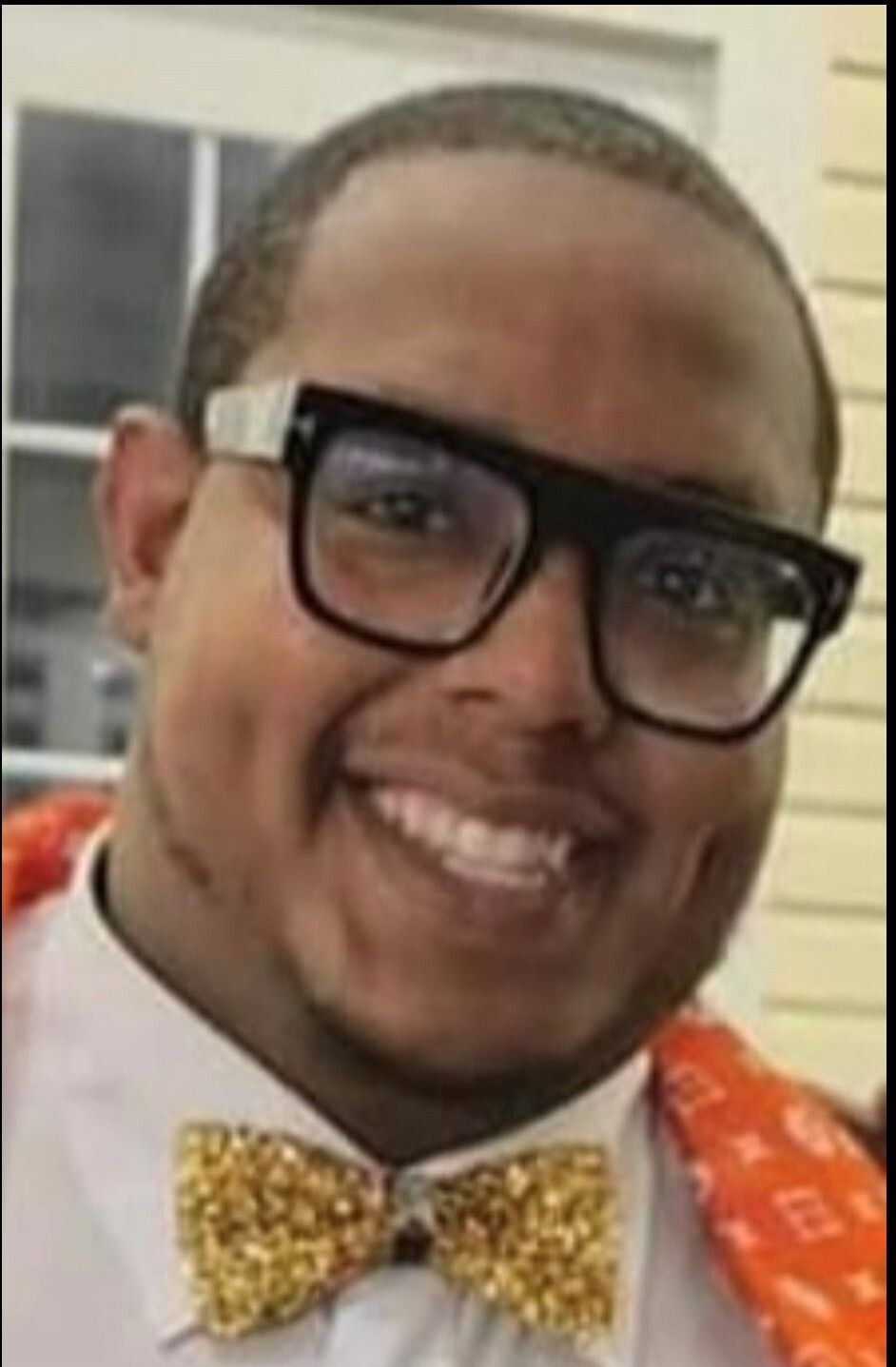 Man with glasses and a gold bow tie smiling.