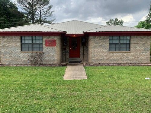 Brick duplex with red trim and door, a concrete path, and green lawn.