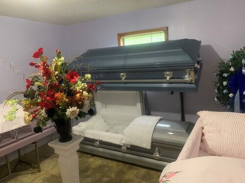 A funeral home interior featuring a blue casket on display and floral arrangements.