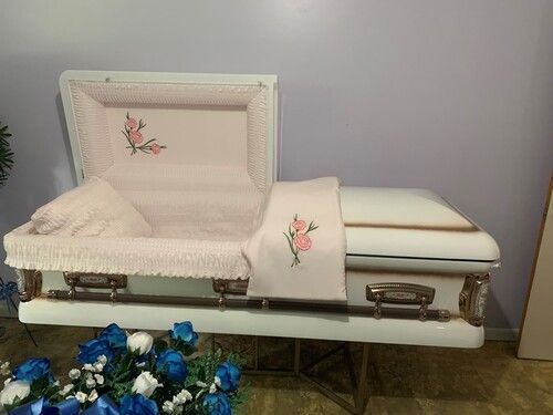 Open white casket with pink floral embroidery on display in a room.