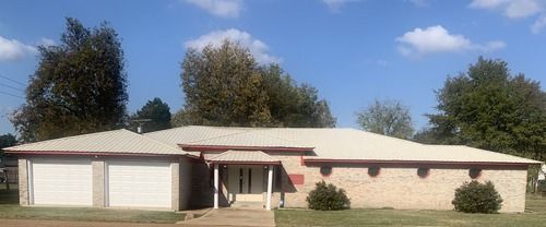 A single-story brick house with two garage doors and a front porch, under a blue sky.