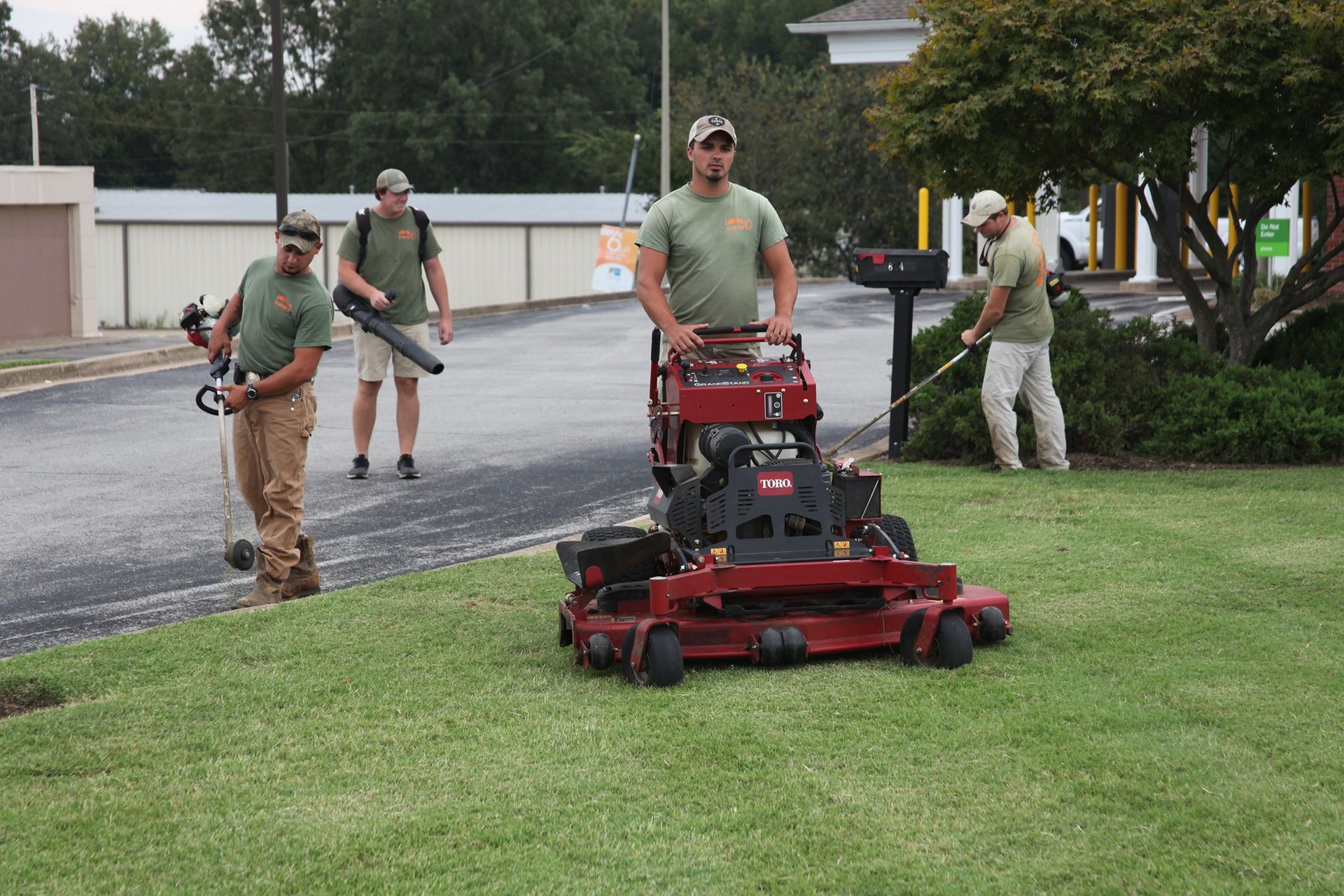 Landscaping crew poses on a grassy lawn with mowers. 