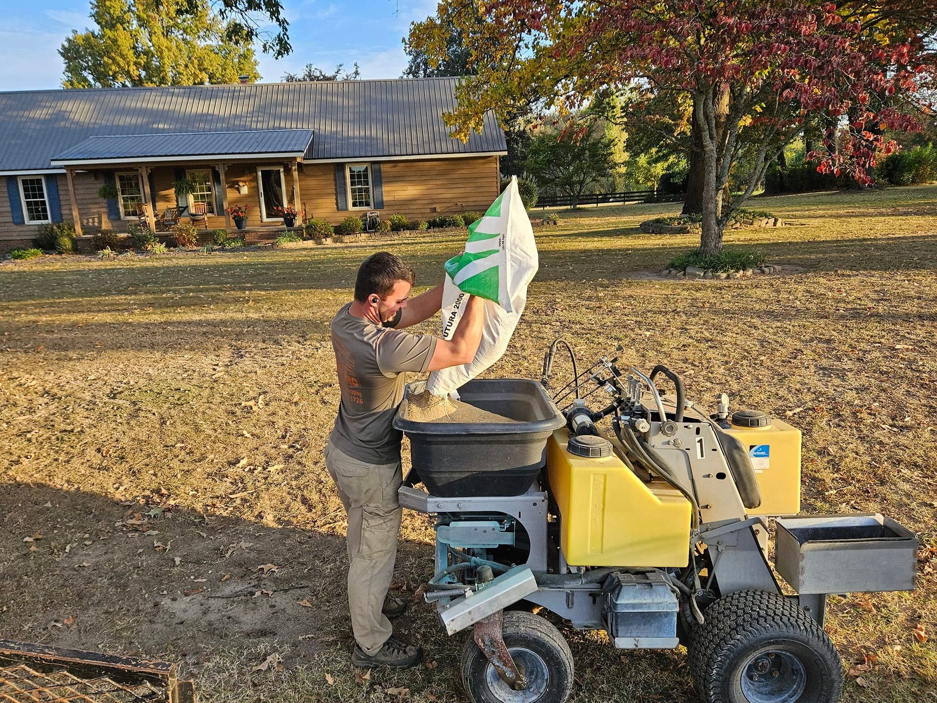 Man filling a seed spreader on a lawn, house in background.