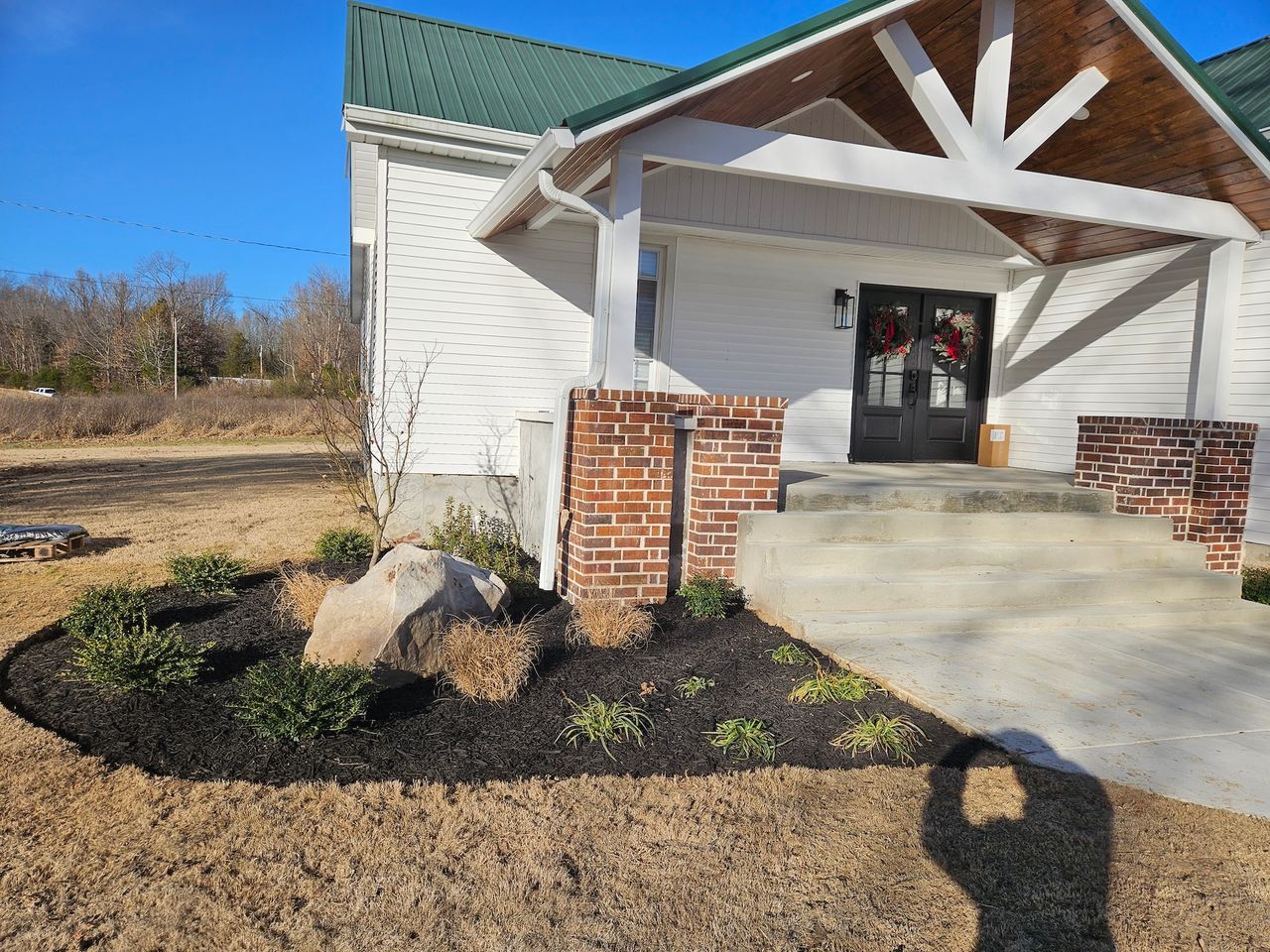 White house with green roof, brick accents, and landscaped front yard with mulch and shrubs.