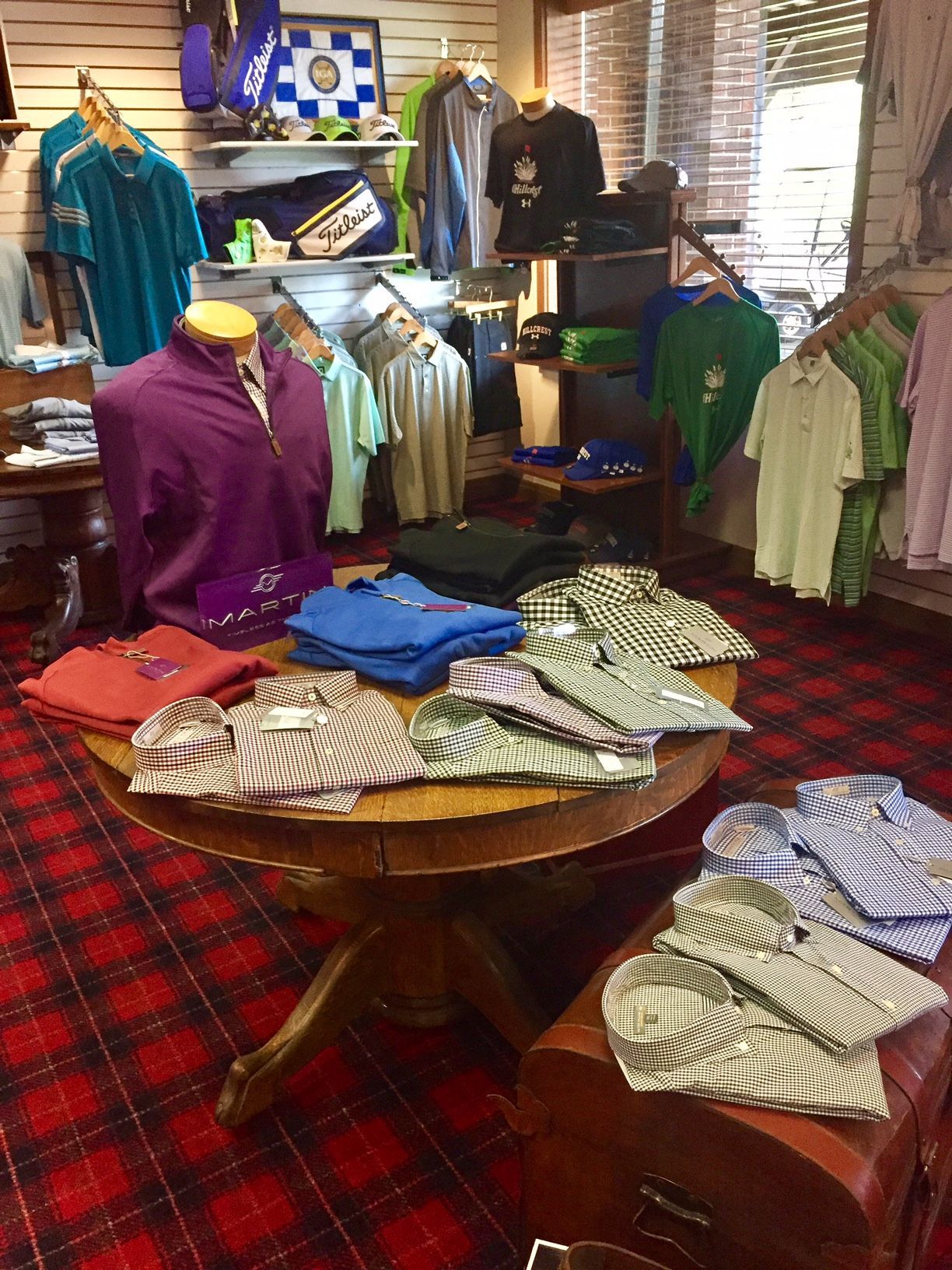 Golf shop interior with polo shirts displayed on a table and shelves; red plaid carpet.