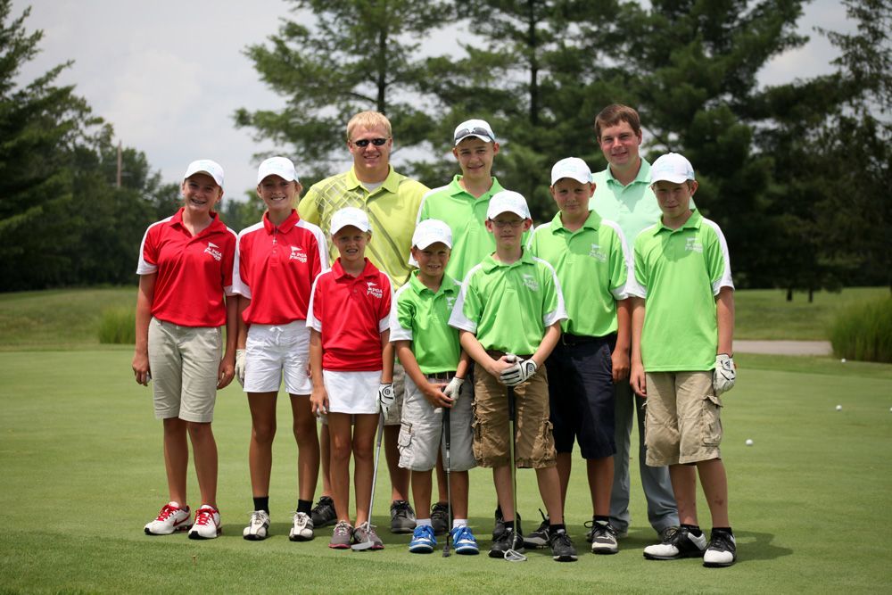 Group of youth golfers in red and green shirts, posing on a green golf course.
