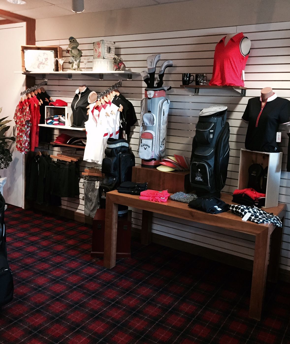 Golf shop interior with clothing, bags, and equipment displayed on shelves and a table; red and black checkered floor.