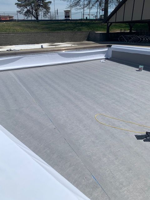 Gray and white flat roof with a white perimeter, yellow cable, and building in the background.