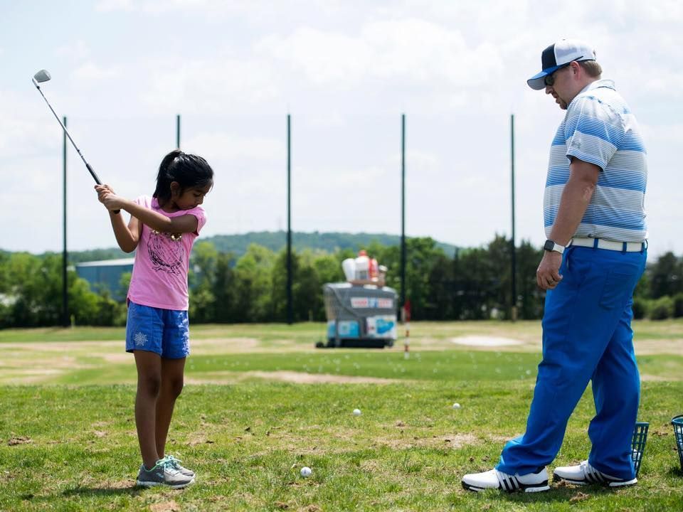 Girl swinging golf club with coach on a sunny golf course.