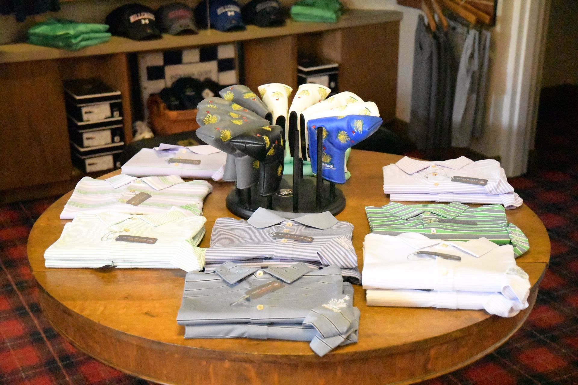 Golf shirts on a round table with golf club head covers displayed. Shop interior.